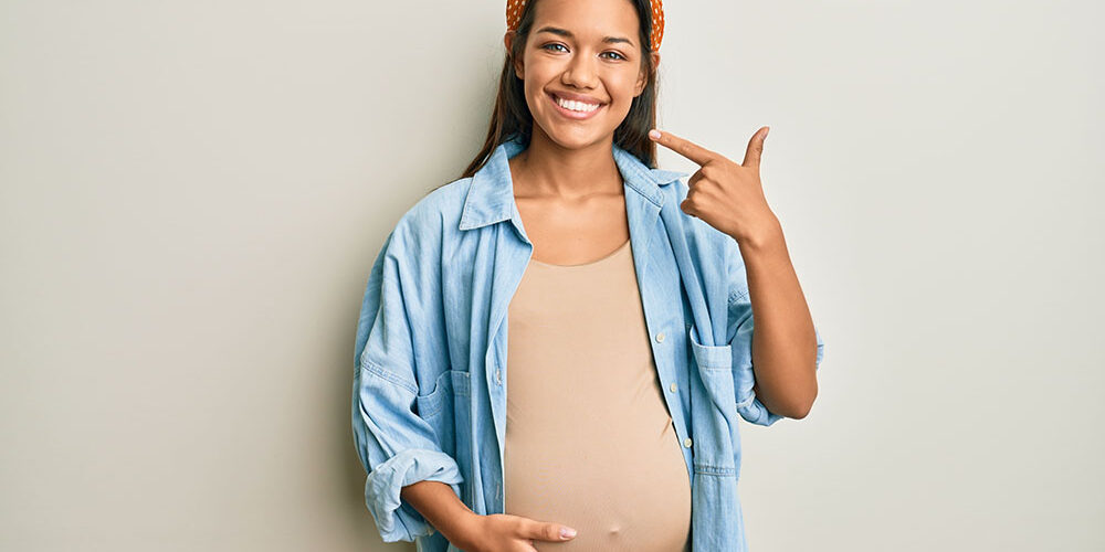 A pregnant girl points to her smile.